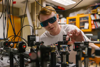 Student adjusts laser optics while wearing protective glasses.