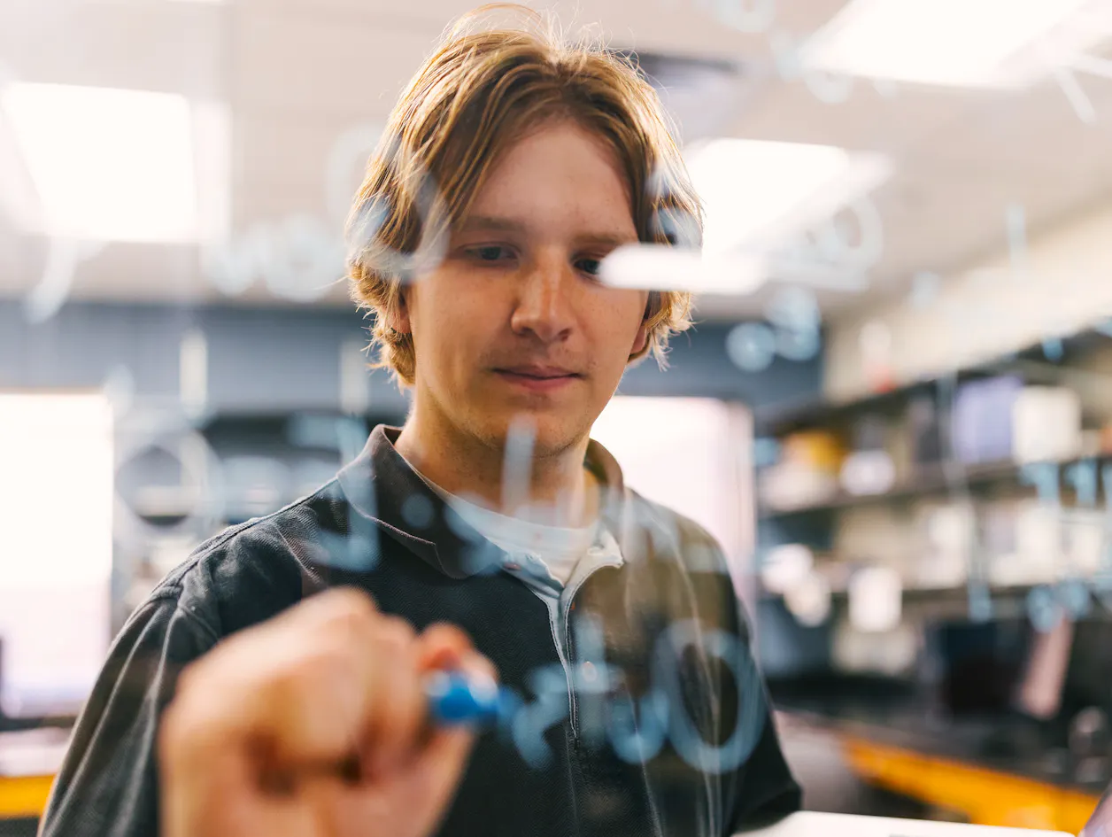Student writes observations on a transparent surface in a physics lab.