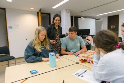 A professor engages with students working on a group project using colorful materials in a Bethel University classroom.