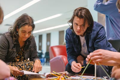 A professor and a student lean over a table, deeply focused on a hands-on project at Bethel University.