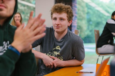 A student attentively listens in a Bethel University classroom, surrounded by peers.