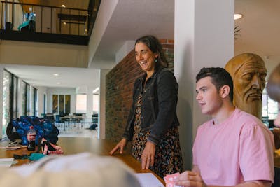 A professor stands smiling while interacting with a student during a classroom session at Bethel University.