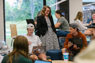 A professor chats with students working on laptops in a casual, open space at Bethel University.