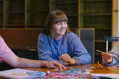 A student smiles while working on a creative project with classmates at Bethel University.