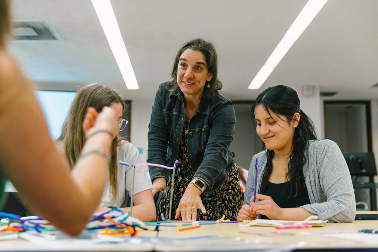 A professor engages with students working on a group project using colorful materials at Bethel University.