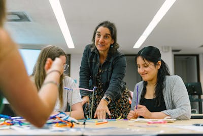 A professor engages with students working on a group project using colorful materials at Bethel University.