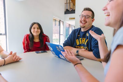 Group of students laughing and chatting around a table, enjoying their time together.