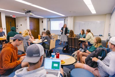 Classroom full of engaged students, professor at the front with a presentation.