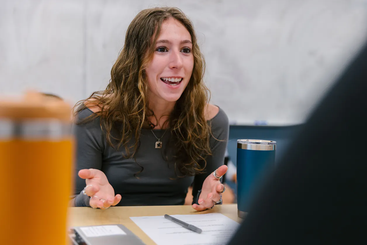 A Bethel University professor gesturing while talking, with students blurred in the foreground.