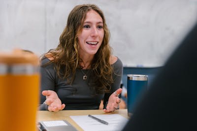 A Bethel University professor gesturing while talking, with students blurred in the foreground.