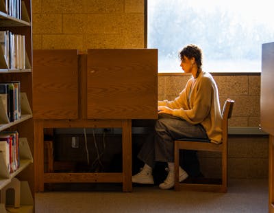 Student studying alone in a quiet library cubicle with bookshelves nearby. 