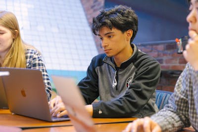 A focused student is typing on a laptop in a group study session. 