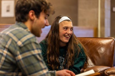 Two students are sharing a laugh while studying together on a cozy leather couch. 