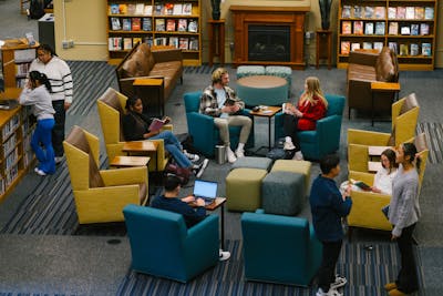 Students are enjoying a vibrant library space with comfortable seating and shelves full of books. 