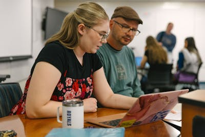 A Bethel University student and professor discussing work on a laptop in a classroom setting.