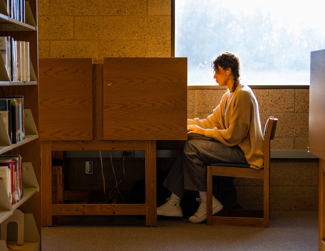 Student studying alone in a quiet library cubicle with bookshelves nearby. 