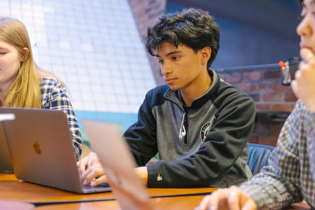 A focused student is typing on a laptop in a group study session. 
