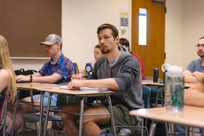 Bethel University students attentively listening and taking notes during a classroom lecture.