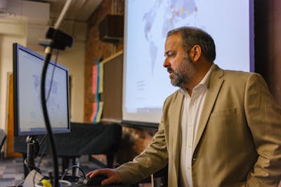 A Bethel University professor explaining a concept using a world map displayed on a large screen.