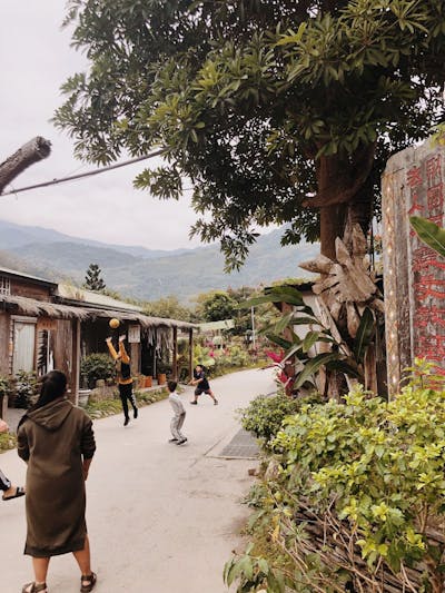 Children playing on a sunny street in a village with lush greenery and mountains.