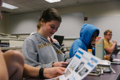 Students in a classroom, one reading a brochure, engaged in individual activities.