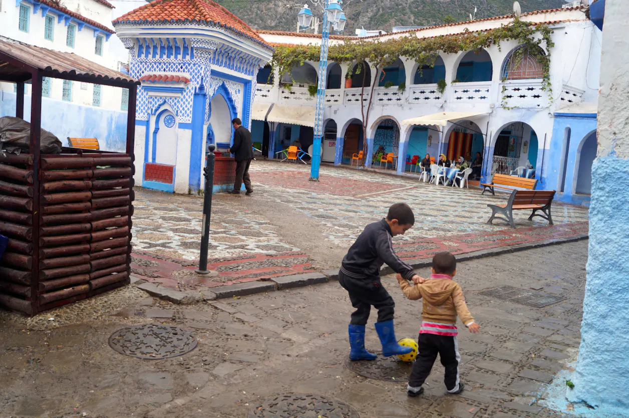 Two children playing in a colorful courtyard, one helping the other with a playful gesture.