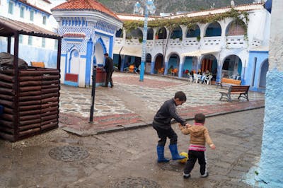 Two children playing in a colorful courtyard, one helping the other with a playful gesture.