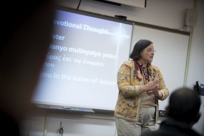 A professor passionately delivers a lecture with a devotional thought displayed on the screen.