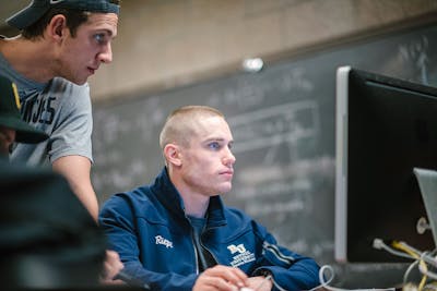 Two students focus on a computer screen while working on a project in a classroom.