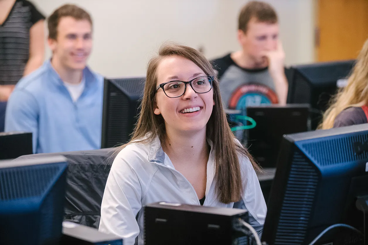 Engaged student smiles while participating in a computer-based class at Bethel University.