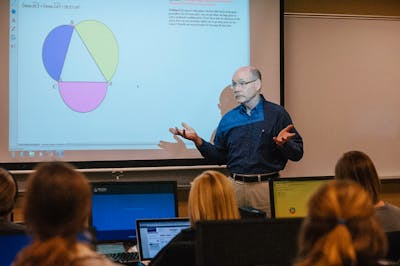 A Bethel University professor explaining a math concept with a colorful diagram on the screen behind him.