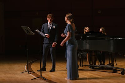 Two students performing a duet on stage with a pianist accompanying them.