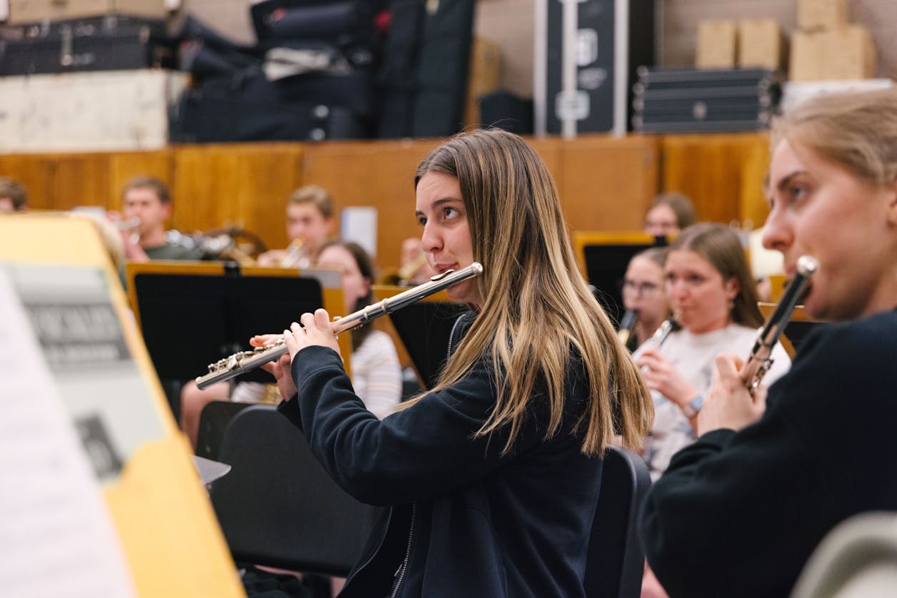 A student playing the flute in a music class, concentrating on her sheet music.