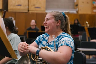 A student laughing while holding her French horn during a music class.