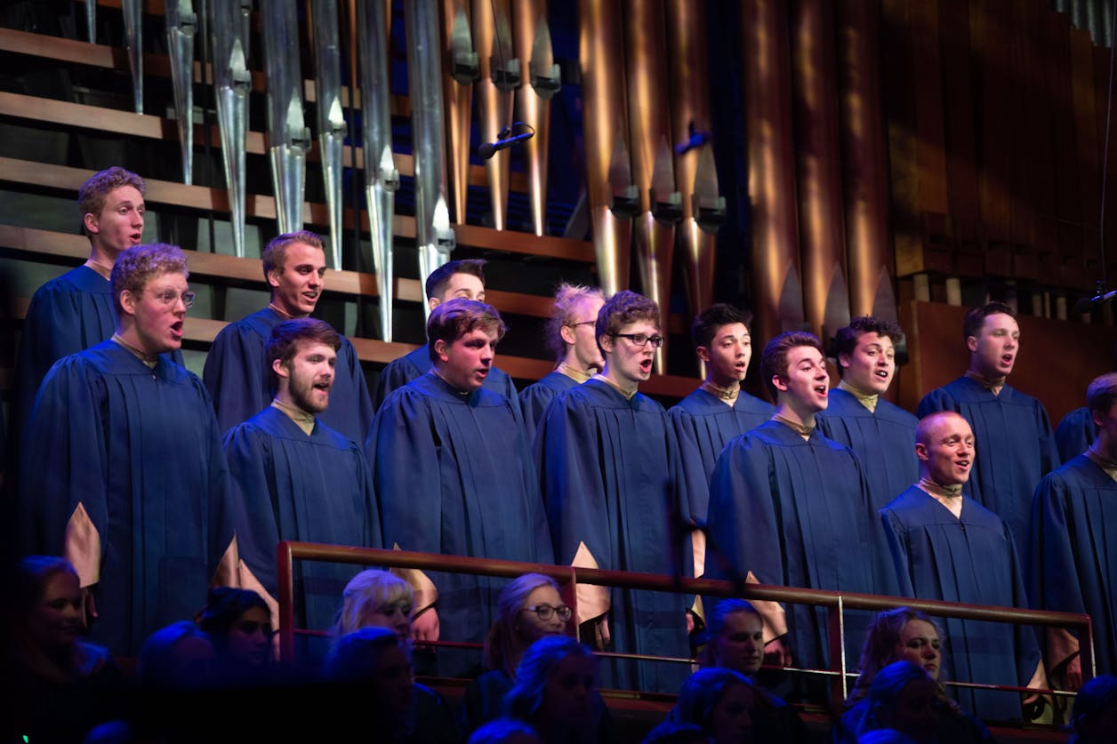 Choir of male students singing in blue robes at Bethel University, harmonizing under dramatic lighting.