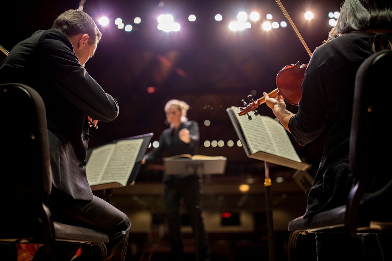 Close-up of violinists playing passionately on stage at Bethel University, with the conductor in the background.