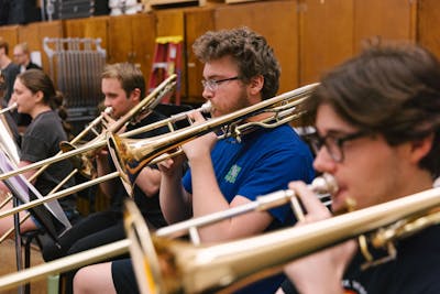 Students passionately playing trombones in a music practice room.