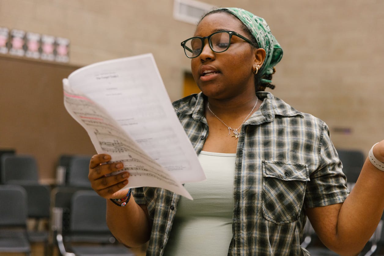 A student singing from sheet music in a classroom, showcasing talent.