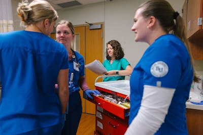 Nursing students and a professor discuss procedures in a Bethel University simulation room.