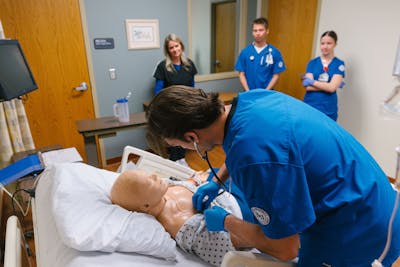 A nursing student practices listening to a mannequin's heartbeat during a Bethel University training session.