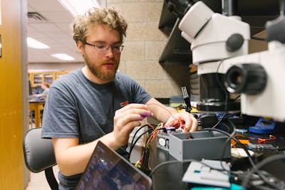 Student working on a technical project, wires and tools spread out on the table.