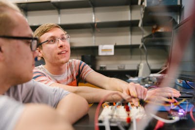 Student in a hoodie works intently on a wiring project in a lab.