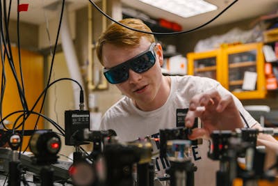 A student wearing protective eyewear focuses intently on a project.