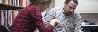 A professor and a student having an in-depth discussion in a book-filled office.