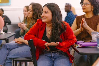 A student in a red shirt smiling and engaging in a lively classroom discussion.