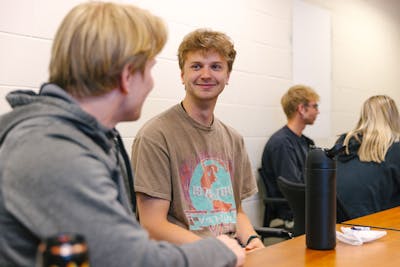 A group of students chatting and smiling in a classroom setting.