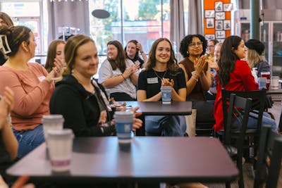 A diverse group of students clapping and smiling during a presentation in a casual setting.