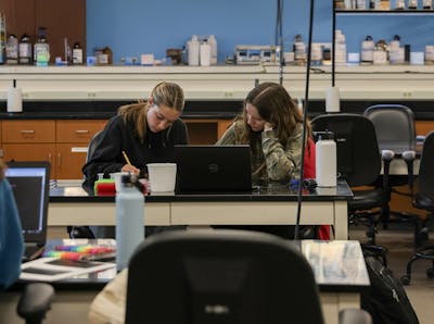 Two students collaborating at a lab table with a laptop and science equipment.