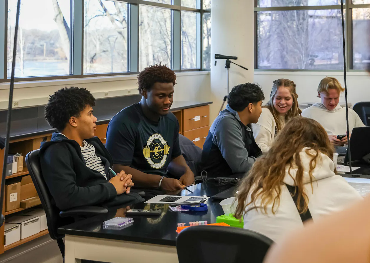 Students chatting and smiling around a lab table during a group activity.
