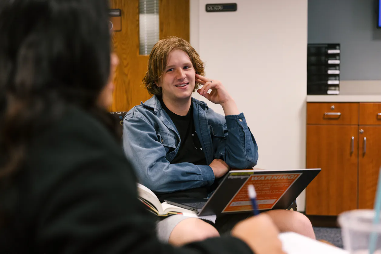 Student in a denim jacket smiling during a classroom conversation at Bethel University.